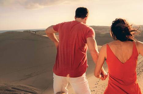 A couple holding hands running over sand dunes