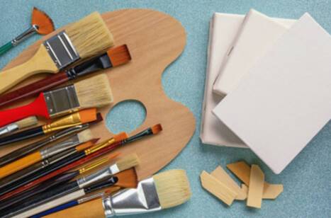 A birds-eye view of art supplies including paint brushes, a palette and canvases