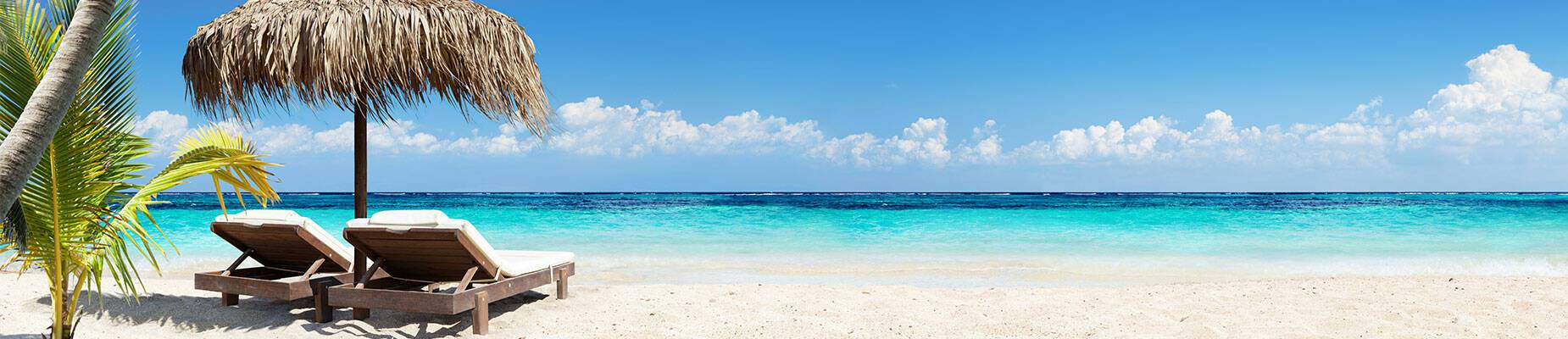 Two sunbeds beneath palm trees on an idyllic Caribbean beach