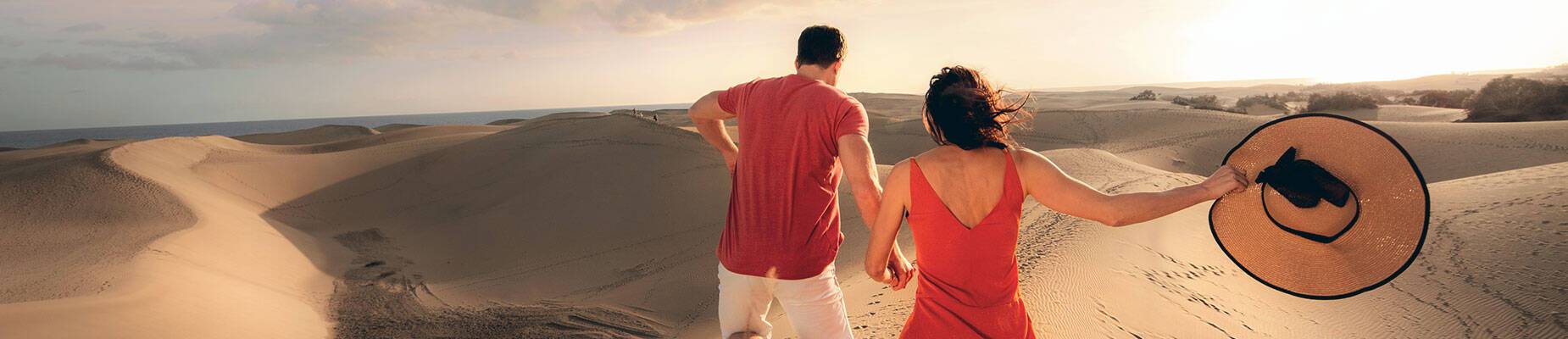 A couple holding hands running over sand dunes