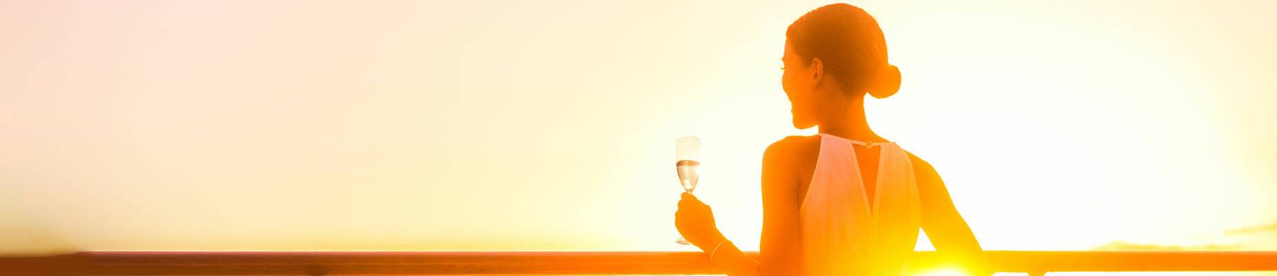 Woman in a dress enjoying a drink at sunset on a cruise ship